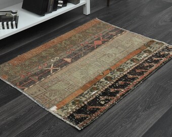 May include: A vintage rug with a muted color palette of brown, green, and orange. The rug has a geometric pattern with a central stripe and a border of intricate designs.