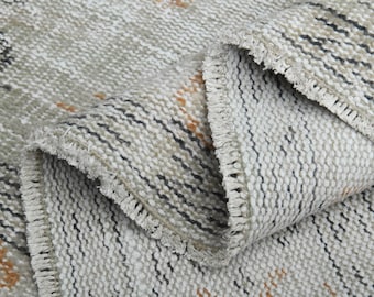 May include: Close-up of a woven rug with a fringe border. The rug has a light gray background with black and orange stripes.