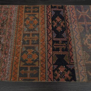 May include: A vintage rug with a geometric pattern in shades of red, brown, black, and blue. The rug has a distressed look and is made of wool.