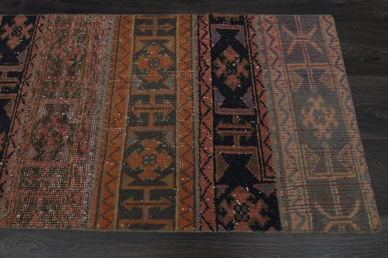 May include: A vintage rug with a geometric pattern in shades of red, brown, black, and blue. The rug has a distressed look and is made of wool.