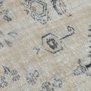 May include: A woven rug featuring a light beige background with a repeating pattern of dark grey geometric shapes, including stylised hexagonal motifs and jagged lines, creating a textured surface with a distressed appearance.