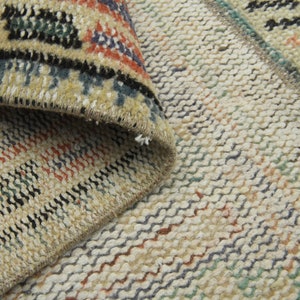 May include: Close-up of a woven rug with a beige background and colorful stripes. The rug has a textured surface and a fringe edge.