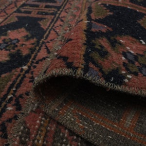 May include: Close-up of a red, black and green patterned rug with a fringed edge. The rug is folded over, showing the underside of the fabric.