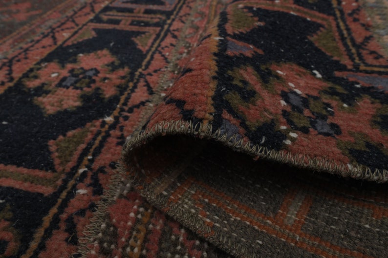 May include: Close-up of a red, black and green patterned rug with a fringed edge. The rug is folded over, showing the underside of the fabric.