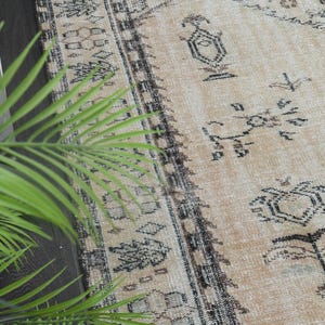 May include: A rectangular area rug featuring a light tan base colour with a dark charcoal grey geometric pattern. The design includes intricate borders and repeating motifs across the surface, showcasing a weathered and textured appearance.