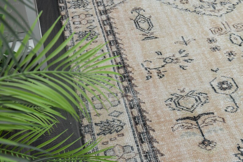 May include: A rectangular area rug featuring a light tan base colour with a dark charcoal grey geometric pattern. The design includes intricate borders and repeating motifs across the surface, showcasing a weathered and textured appearance.