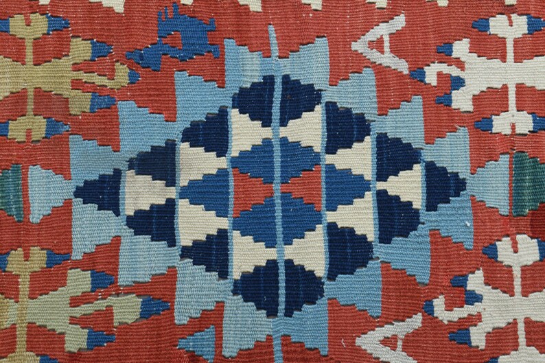 K&ouml;nnte beinhalten: Eine Nahaufnahme eines bunten gewebten Teppichs mit einem geometrischen Muster in Rot-, Blau-, Wei&szlig;- und Beiget&ouml;nen. Der Teppich hat eine zentrale Diamantform mit komplizierten Details.