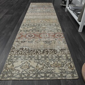 May include: A beige, brown, and red patterned runner rug with a floral design. The rug has a distressed look and is made of woven fabric.