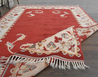 May include: A red rug with a cream-coloured border and floral pattern. The rug has a fringe on the edges and is folded in half.