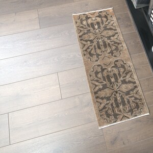 May include: A brown and black patterned runner rug with a geometric design. The rug is on a light wood floor.