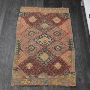 May include: A rectangular, hand-woven rug with a geometric diamond pattern in shades of red, beige, and gray. The rug has a traditional design, suitable for a hallway or small space. The rug's dimensions are approximately 24 x 36 inches.