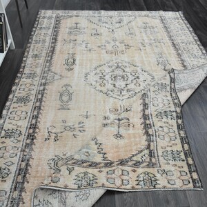 May include: A rectangular area rug featuring a light beige base with intricate dark grey and muted blue geometric patterns, including a central medallion and a detailed border, with one corner folded over to reveal the underside.