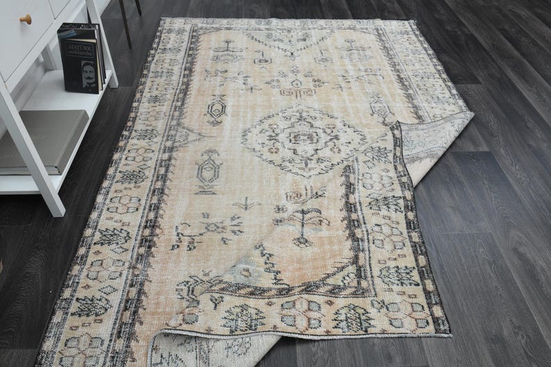 May include: A rectangular area rug featuring a light beige base with intricate dark grey and muted blue geometric patterns, including a central medallion and a detailed border, with one corner folded over to reveal the underside.