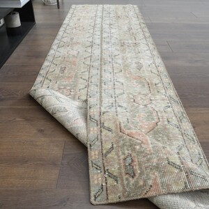 May include: A light beige and gray vintage runner rug with a geometric pattern. The rug is rolled up and partially unfurled, showing the intricate details of the design.