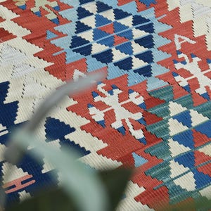 K&ouml;nnte beinhalten: Nahaufnahme eines bunten gewebten Teppichs mit einem geometrischen Muster in Rot-, Blau-, Wei&szlig;- und Gr&uuml;nt&ouml;nen. Der Teppich hat ein traditionelles Design mit filigranen Details.