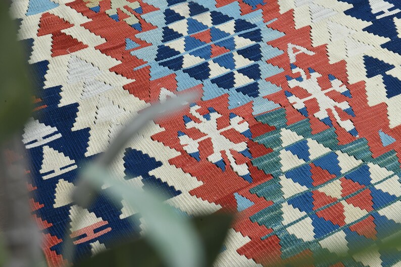 K&ouml;nnte beinhalten: Nahaufnahme eines bunten gewebten Teppichs mit einem geometrischen Muster in Rot-, Blau-, Wei&szlig;- und Gr&uuml;nt&ouml;nen. Der Teppich hat ein traditionelles Design mit filigranen Details.