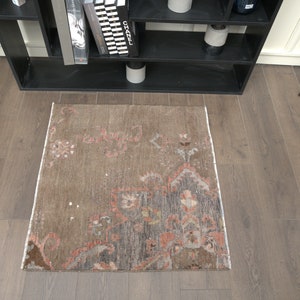 Könnte beinhalten: Ein brauner und grauer Teppich mit einem verblassten Blumenmuster. Der Teppich hat einen Fransenrand und liegt auf einem Holzboden.