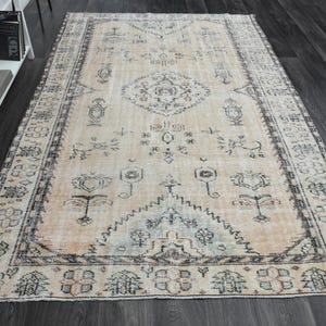 May include: A rectangular area rug featuring a light peach background with intricate dark grey and muted blue geometric and floral patterns. The design includes a central medallion, symmetrical motifs, and a detailed border frame.