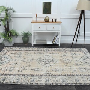 May include: A rectangular area rug featuring a light beige base with a faded, intricate pattern in shades of charcoal grey and muted blue. The design includes a central medallion surrounded by symmetrical floral and geometric motifs.