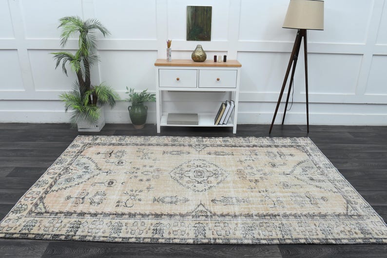 May include: A rectangular area rug featuring a light beige base with a faded, intricate pattern in shades of charcoal grey and muted blue. The design includes a central medallion surrounded by symmetrical floral and geometric motifs.