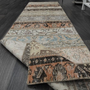 Könnte beinhalten: Ein rechteckiger, mehrfarbiger Läufer mit Patchwork-Design. Der Teppich weist verschiedene Muster und Farben auf, darunter Beige, Orange, Blau und Braun. Der Teppich ist teilweise aufgerollt und zeigt seine Unterseite.