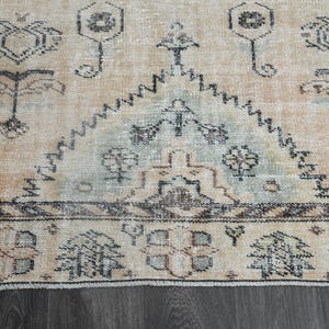 May include: A woven area rug featuring a light peach background with dark grey geometric and floral patterns. The design includes a central triangular motif with intricate borders and symmetrical shapes throughout the textile surface.