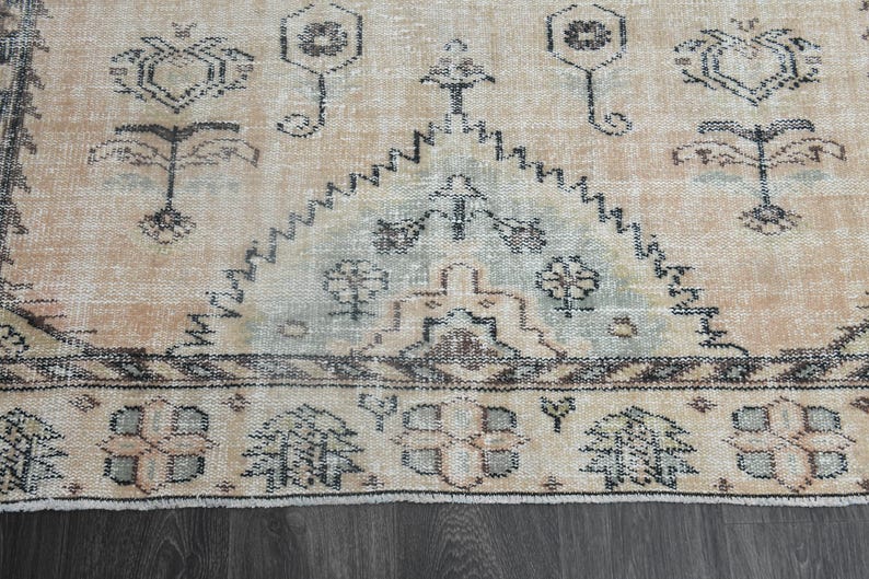 May include: A woven area rug featuring a light peach background with dark grey geometric and floral patterns. The design includes a central triangular motif with intricate borders and symmetrical shapes throughout the textile surface.