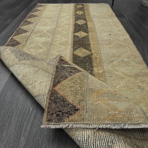 Könnte beinhalten: Ein beige-brauner Teppich mit geometrischem Muster. Der Teppich ist in der Mitte gefaltet und die Fransen sind sichtbar.