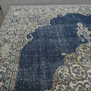 May include: A vintage rug with a navy blue center and a cream-colored border with intricate floral patterns. The rug has a distressed, faded look, giving it a unique and antique feel.