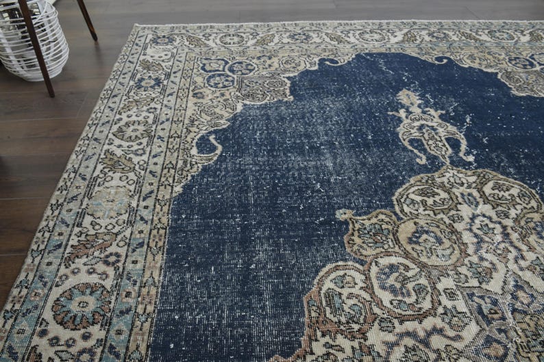 May include: A vintage rug with a navy blue center and a cream-colored border with intricate floral patterns. The rug has a distressed, faded look, giving it a unique and antique feel.