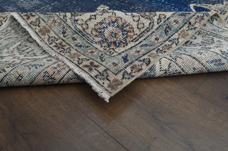 May include: A close-up of a folded rug with a blue and cream patterned design. The rug is folded over on itself, revealing the underside of the rug.