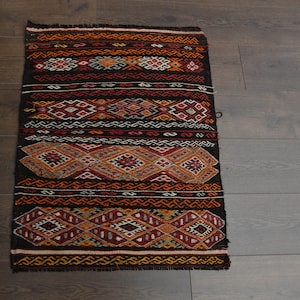 May include: A black and red patterned rug with geometric designs. The rug has a fringe border and is made of wool.