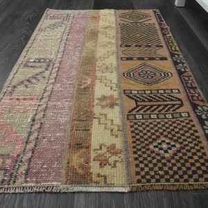 May include: A vintage Turkish rug with a geometric pattern in shades of pink, beige, and brown. The rug has a fringed edge and is made of wool.