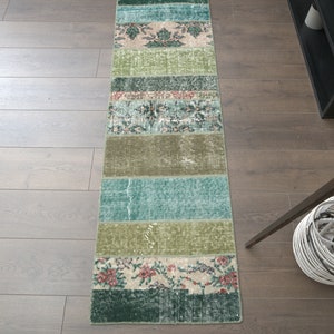 May include: A long, rectangular runner rug with a patchwork design. The rug is made of different colored fabrics, including green, blue, and beige. The rug has a floral pattern and is perfect for adding a touch of color and style to any room.