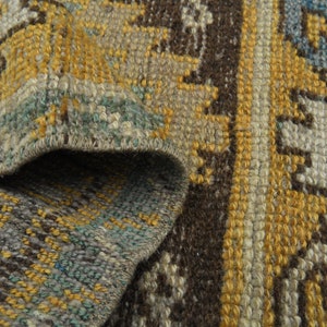 May include: Close-up of a woven rug with a brown, yellow, and blue geometric pattern. The rug has a frayed edge and a textured surface.