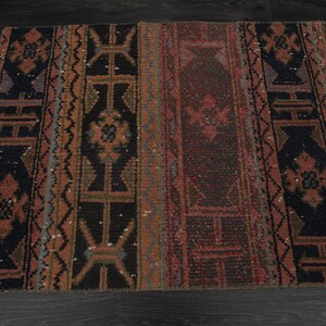 May include: A vintage rug with a geometric pattern in shades of red, brown, and black. The rug has a distressed look and is made of wool.