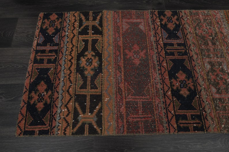 May include: A vintage rug with a geometric pattern in shades of red, brown, and black. The rug has a distressed look and is made of wool.