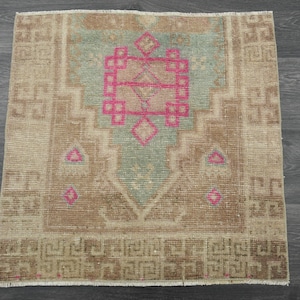 May include: A vintage rug with a faded brown and green color scheme. The rug has a central design with pink accents and a geometric pattern.