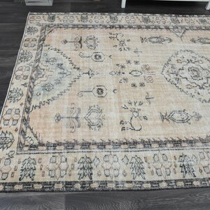 May include: A rectangular area rug featuring a faded peach and beige background with intricate dark grey geometric and floral patterns. The rug has a wide border with repeating motifs and a central medallion design in a muted colour palette.