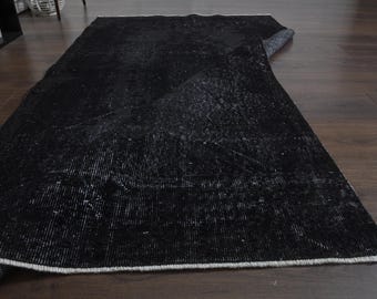 Pode incluir: Um tapete preto e branco desgastado com formato retangular. O tapete tem uma aparência vintage desbotada com uma borda branca. O tapete está parcialmente enrolado, revelando a parte inferior.