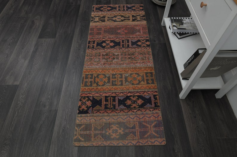 May include: A long, narrow rug with a colourful geometric pattern in shades of red, orange, brown, and black. The rug has a traditional, ethnic design.
