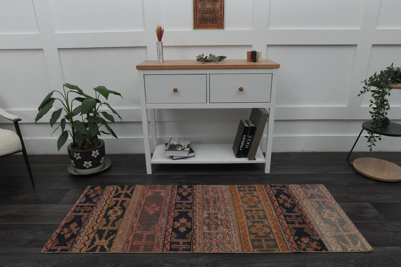 May include: A white console table with two drawers and a lower shelf. The table has a wood top and is decorated with a small potted plant, books, and a rug with a colourful geometric pattern.
