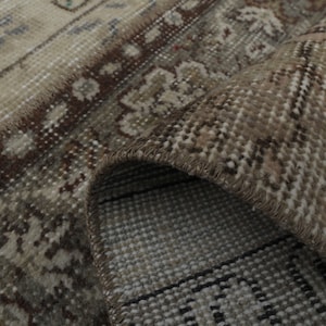 May include: Close-up of a beige and brown patterned rug with a fringe border. The rug is folded over, revealing the woven backing.