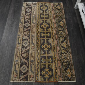 Op de afbeelding: Een vintage tapijt met een geometrisch patroon in tinten bruin, beige en goud. Het tapijt heeft een vervaagde, verweerde uitstraling, waardoor het een unieke en antieke uitstraling heeft.