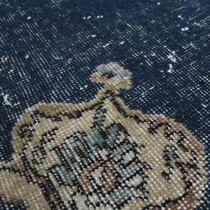May include: Close-up of a blue rug with a beige pattern. The rug has a distressed look with faded areas and a worn texture.