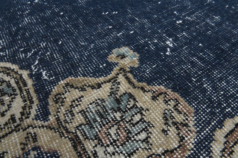 May include: Close-up of a blue rug with a beige pattern. The rug has a distressed look with faded areas and a worn texture.