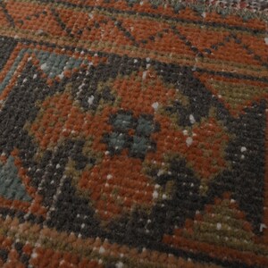 May include: Close-up of a rug with a geometric pattern in shades of brown, orange, green, and blue. The rug has a worn, vintage look.