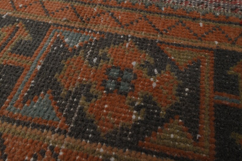 May include: Close-up of a rug with a geometric pattern in shades of brown, orange, green, and blue. The rug has a worn, vintage look.