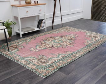 May include: A rectangular area rug featuring a large central medallion in shades of cream, brown, and teal set against a dusty pink field. The border displays intricate floral and vine patterns in teal, orange, and cream tones.