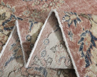 May include: Close-up of the edge of a rug with a beige and red patterned design. The rug has a white fringe.